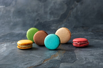 Colorful assorted french macaroons on dark stone background. Side view