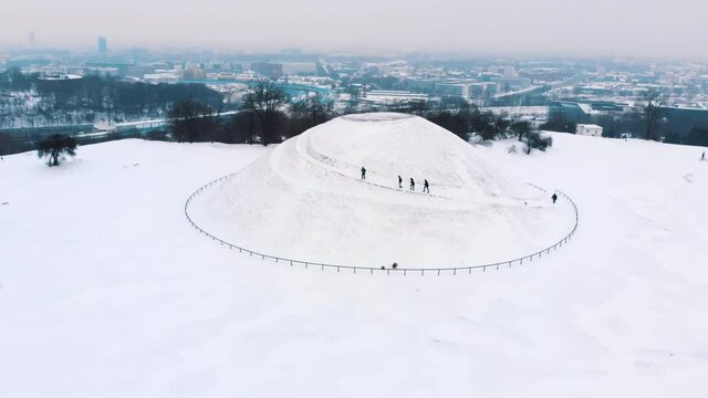 Group of hikers on Kopiec krakusa (Krak Mound) covered with snow in Krakow, Poland. Winter season with light snow fall. Snowy landscape with grove of trees in the background. 