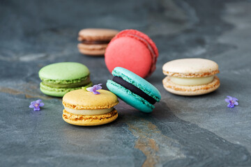 Colorful assorted french macaroon cakes on dark stone background. Side view