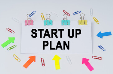 On the table there are paper clips and directional arrows, a sign that says - Start Up Plan