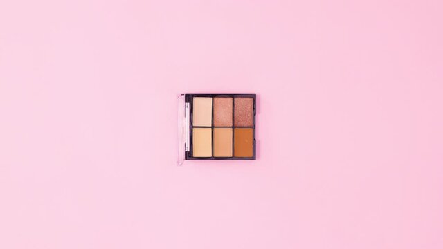 Eye shadow palette rotating on pastel pink background. Stop motion flat lay