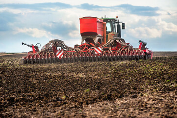 Fototapeta premium Farmers sow, using tractor with seeder in a plowed field, apply fertilizer, sowing time