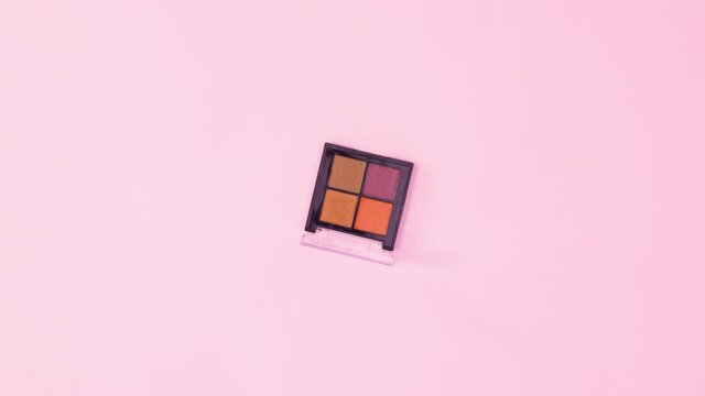 Eye shadow palette rotating on pastel pink background. Stop motion flat lay