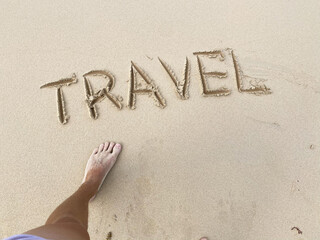 Travel inscription with person's leg on summer sandy beach. Vacation and adventure concept