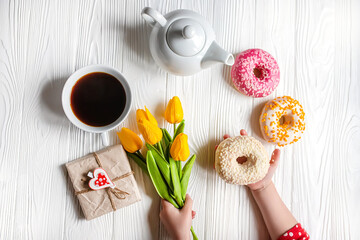 The child's hands holding a bouquet of tulips and a doughnut. Romantic Valentine's day Breakfast in bed for your loved one. concept of mothers Day, 8 March. Flat lay. Top view