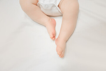 Laying in bed sheet baby infant feet toes, wearing white bodysuit with buttons, tender skin, barefoot newborn child