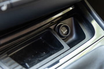 Electronic cigarette lighter on car dashboard console along with ash tray for smoking while driving.