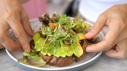 Hands picking a healthy organic gluten free toast with sliced avocado and vegetables on it