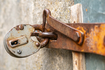 The padlock is hanging on the door. A large barn lock on a rusty door hinge.