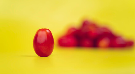Horizontal photo, in a yellow background, of a cherry tomato with a somewhat unusual shape. In the background other tomatoes.