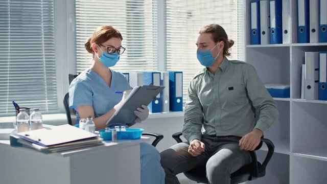 man wearing medical mask being examined by female medical worker in hospital office before being vaccinated against virus and infection