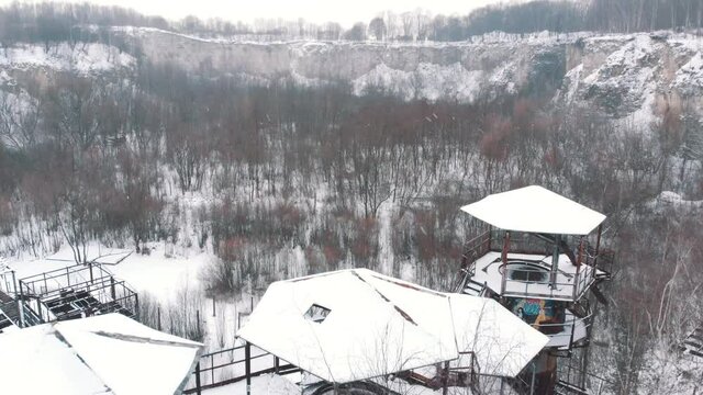 Aerial footage of Liban Quarry - A historic site where prisoners were kept during Second World War. Old machines and piping equipment. Light snow-fall. Grove of trees can be seen. 