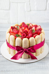 Delicious fresh classic tiramisu dessert   with strawberries and Savoiardi biscuits,  biscuit dipped in coffee and cream of mascarpone cheese. Decorated with  red bow.