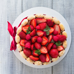 Delicious fresh classic tiramisu dessert   with strawberries and Savoiardi biscuits,  biscuit dipped in coffee and cream of mascarpone cheese. Decorated with  red bow. View from above.