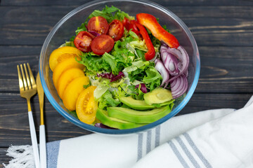 Fresh green salad with avocado, tomatoes, pepper, onion in big white bowl on wooden tray. Vegan salad with green mix leaves and vegetables. Top view on gray table. Healthy vegetarian food. Close up