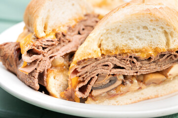 Beef dip sandwich, shaved roast beef, mushrooms, and bacon, on a baguette bun.