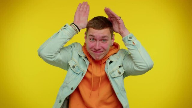 I am little bunny rabbit. Lovely funny teen boy 20s years old smiling friendly and doing bunny ears gesture on head, having fun, fooling with humorous comical mood. Young man on yellow background