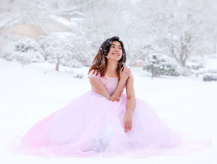 Fototapeta na wymiar Teen girl in pink formal gown sitting outdoors in snow