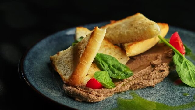 White bread toast, sliced with triangle and pate, decorated with spinach and cherry tomatoes on a gray plate on a black background.