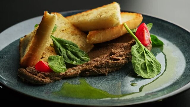 White bread toast, sliced with triangle and pate, decorated with spinach and cherry tomatoes on a gray plate on a black background.