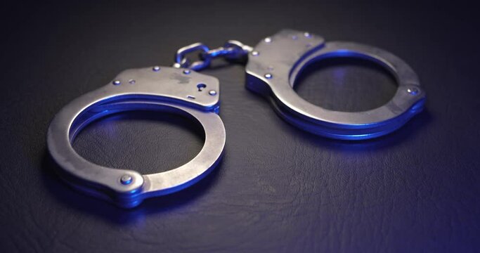 Pair of handcuffs used by law enforcement to arrest criminals, lit in red and blue flashing police lights. Justice or catching a guilty criminal concept.