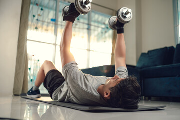 Young man use dumbbell exercises chest fly on yoga mat in living room at home. Fitness, workout and...