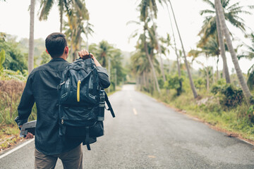 rear view of man with backpack hiking and walking on the road in forest. Backpack travel concept.