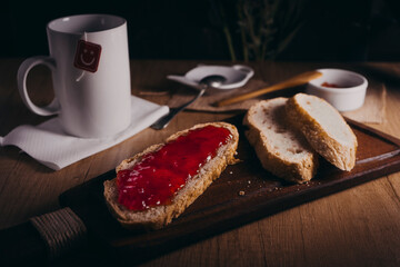 Slices of homemade bread on a table. One of the slices is smeared with tomato jam, there is also a cup of tea. Breakfast or snack concept.