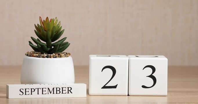Wooden calendar with an important event for September 23, a woman's hand sets the date on the calendar. Autumn season.	