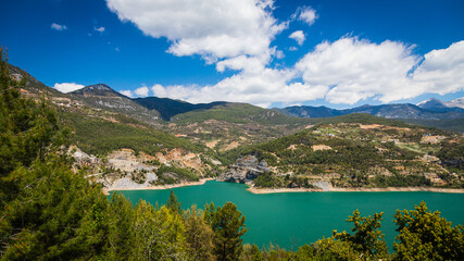 Fototapeta na wymiar Panoramic view of a mountain lake with clear turquoise-green water against the background of a road and a village of farmers