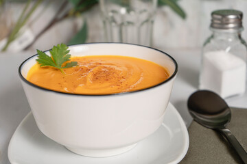 Side view of a white bowl with butternut squash and carrot cream soup. Natural and healthy eating concept.