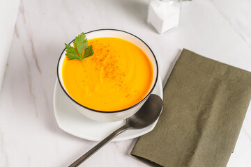 Chopped view of a white bowl with cream of squash and carrots soup with a green napkin. Natural and healthy eating concept.