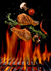 Chicken legs and spicy ingredients flying above flaming red barbeque grill