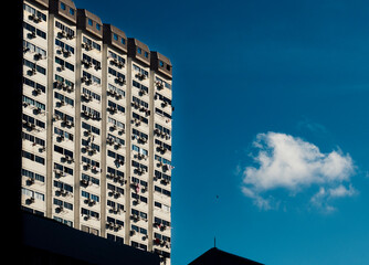 Fototapeta premium Old Asian apartment blocks with air-conditioning compressors on the outside façade of each unit against a blue sky with a lone cloud