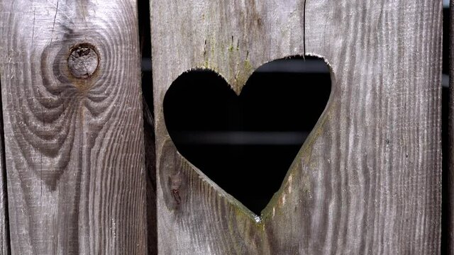 Snow is falling on the background of a heart carved in a wooden door