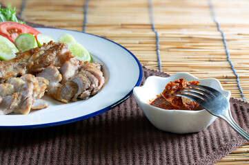 Grilled pork in white dish and chili sauce in cup on  dark brown napery, and brown mat