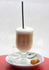 Cappuccino in a glass cup with a straw and cookies on a saucer. Delicious sweet dessert.