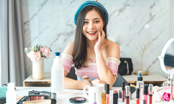 Portrait of young asian woman review cosmetics prosduct face mask fan following channel, recording video make up lipstic cosmetic at home. Beauty blogger present beauty cosmetics.