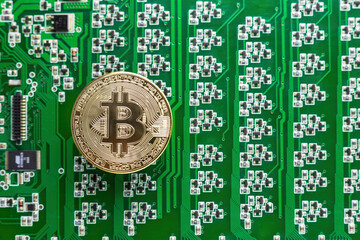 Gold bitcoin coin on the background of a green circuit board with many transistors