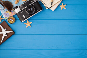 Overhead photo of camera starfish notepad pen sunglasses map plane and compass isolated on the blue wooden background with blank space