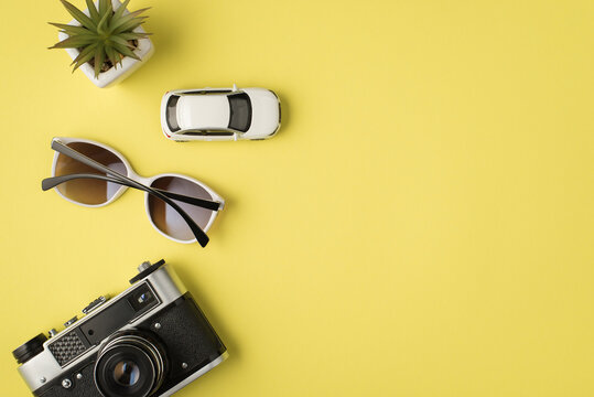 Top view photo of plant car model sunglasses and camera on isolated pastel yellow background with copyspace