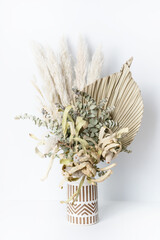 Beautiful dried flower arrangement in a stylish vase. In the flower bunch is Banksia, Palm Frond, Eucalyptus leaves, Bunny tails and Pampas grass, photographed on a white background.