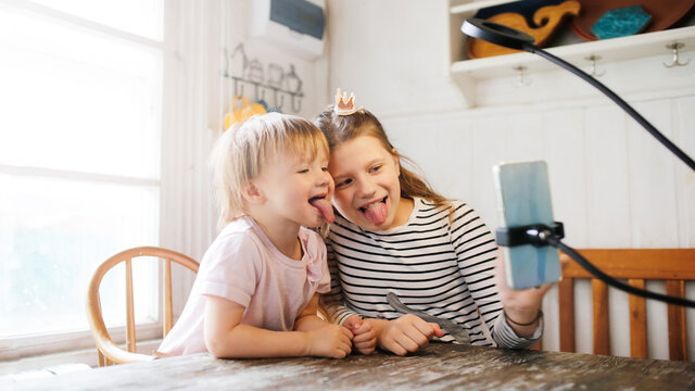 Cute Influencer Young Kids Bloggers Recording Video Blog Show Tongues. Caucasian Funny Children Sisters Play With Phone, Video Call With Phone And Tripod