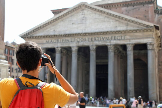 young tourist with backpack on his shoulders while photographing the ancient temple called Pantheon in Rome Italy