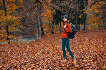 travel tourism and a young woman with a backpack walks in the park in nature landscape tall trees fallen leaves river