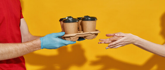 Fototapeta na wymiar Courier in protective gloves giving coffee cups to customer