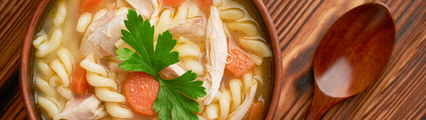 Close-up of a bowl of chicken noodle soup with spoon on a wooden background banner