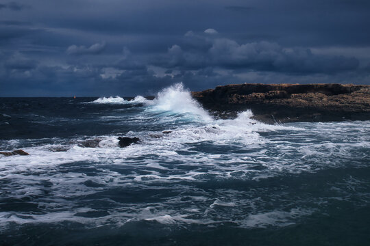 Waves crashing over the rocks on a stormy day in Qawra, Malta. © Kari