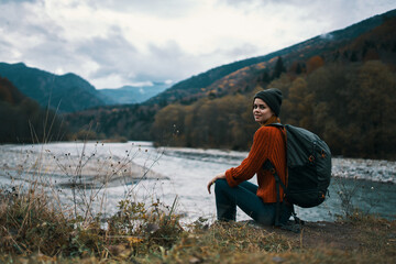 woman near the river in the mountains with a backpack on her shoulders are resting in the autumn forest