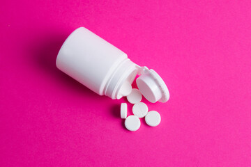 White pills and jar on pink paper background copy space top view